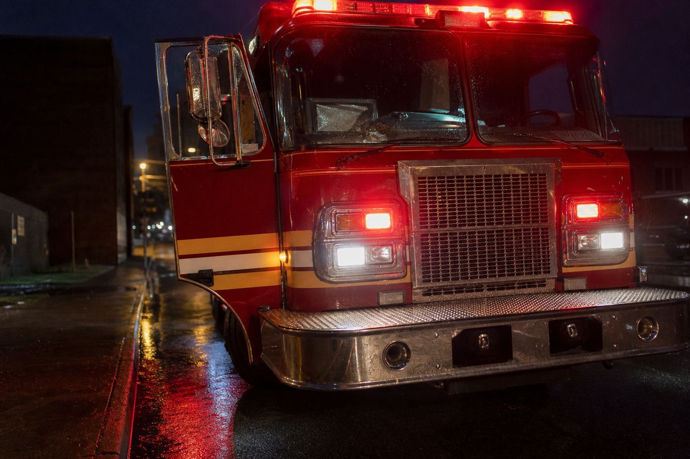 A red fire truck parked outside a small-town police station at night with emergency lights visible in the background